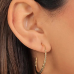 A lifestyle profile photograph of a model's ear featuring a large, elegant open C-shaped hoop earring finished in a polished gold color, characterized by a delicate, continuous beaded or textured ball-chain pattern along the entire curve of the slim band