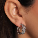A professional on-ear lifestyle photograph showcasing a textured medium-sized hoop earring finished in a polished silver color, featuring a repeating, geometric scalloped marquis pattern densely filled with clear micro-pavé crystals