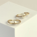 18k gold-tone slender hoop earrings encrusted with pavé crystals, featuring a lustrous white pearl that appears to float within the center of the ring