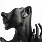 A professional product display photograph featuring an upward-sweeping cluster earring finished in a polished silver color, styled on a matte black mannequin bust to showcase how the asymmetric mosaic of marquise and round clear crystals gracefully climbs and contours the earlobe
