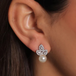 A professional ear-lifestyle photograph showcasing a delicate statement drop earring finished in a polished silver color, featuring a three-petal fleur-de-lis crystal crown stud that suspends a perfectly round, lustrous white pearl drop