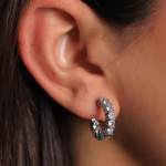 A professional lifestyle photograph of a model showcasing a classic, high-brilliance eternity huggie hoop earring finished in a polished silver color, featuring a continuous front-facing row of shared-prong round brilliant-cut clear crystals that contour closely around the earlobe