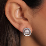 A professional lifestyle photograph of a model showcasing a pair of structured, rectangular post stud earrings in a bright silver color. The earrings feature a tight inner mosaic of step-cut clear baguette crystals enclosed within a shimmering rectangular frame of micro-pavé stones, sitting flush on the earlobe.