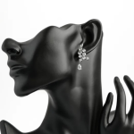 A professional product display photograph of an asymmetric cascading drop climber earring finished in a high-shine silver color, styled on a matte black mannequin bust to highlight the organic vine of round brilliant clear crystals climbing the earlobe, anchored by a freely dangling pear-cut teardrop crystal