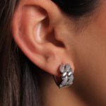 A professional close-up ear model photograph showcasing a bold, chunky huggie hoop earring finished in a high-shine silver color, featuring a heavy interlocking curb chain link design where the braided metal surfaces alternate between a smooth mirror polish and a dense clear crystal pavé setting