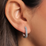 A professional close-up ear model photograph showcasing a medium-sized huggie hoop earring finished in a polished silver color, featuring two symmetrical, parallel rows of micro-pavé crystals running seamlessly along the front curve