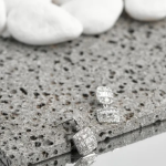 A pair of silver-tone drop earrings featuring a tiered design with rectangular baguette crystals framed by sparkling micro-pavé stones, set against a natural stone background