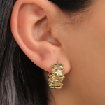 A professional lifestyle photograph of a chunky, wide huggie hoop earring finished in a rich, warm gold color, featuring a highly tactile, stacked accordion ribbed texture that wraps closely around the earlobe