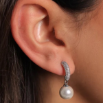 A delicate silver-tone earring featuring a shimmering pavé-encrusted huggie hoop suspending a single, lustrous white pearl drop