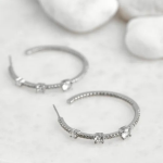 A pair of silver-tone hoop earrings featuring a dainty pavé band punctuated by three sparkling, larger bezel-set crystal stations