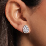 A close-up lifestyle photograph of a model wearing a luxurious, vintage-inspired pear-shaped silver-colored stud earring, featuring a dense cluster of brilliant white stones bordered by a delicate micro-pavé halo