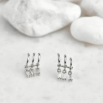 A pair of delicate, silver-tone stud earrings featuring three tiny, linked hoops, each suspending a singular, glistening baguette-cut crystal drop
