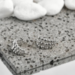 A pair of silver-tone huggie earrings featuring a stacked, triple-row beaded design, displayed on a textured stone surface