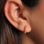 A pair of gold-colored huggie hoops featuring a continuous row of small, bezel-set pear crystals following the curve of the earring
