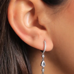 A sophisticated silver-colored huggie hoop featuring a shimmering pavé-lined band and a vertical drop of three graduated round and pear-cut crystals