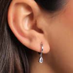 A minimalist silver-colored huggie hoop earring featuring a single, brilliant pear-cut crystal pendant in a classic three-prong setting