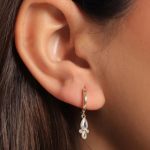 A sophisticated gold-colored huggie hoop featuring a pear-cut crystal pendant accented by a decorative trio of smaller round bezel-set stones at the base