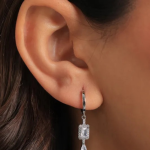 A close-up of a model wearing a thick, wide silver-colored huggie hoop earring completely lined with three rows of glittering micro-pavé crystals
