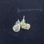 A pair of gold-tone stud earrings featuring a central pear-cut crystal surrounded by a white enamel halo, set against a dark velvet background